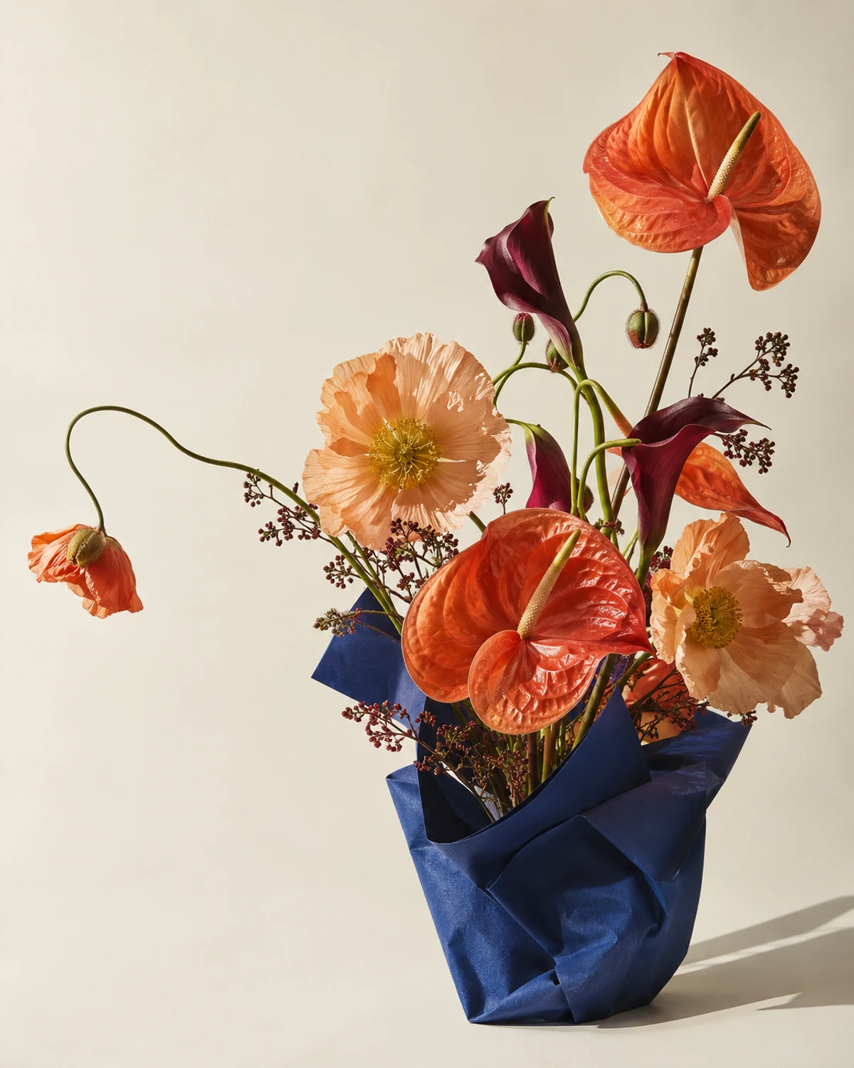 Ramo escultórico de flores coral y burdeos en papel azul.